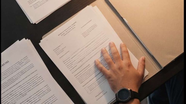 Una mano appoggiata su alcuni documenti, sul tavolo dello sportello di Dama service